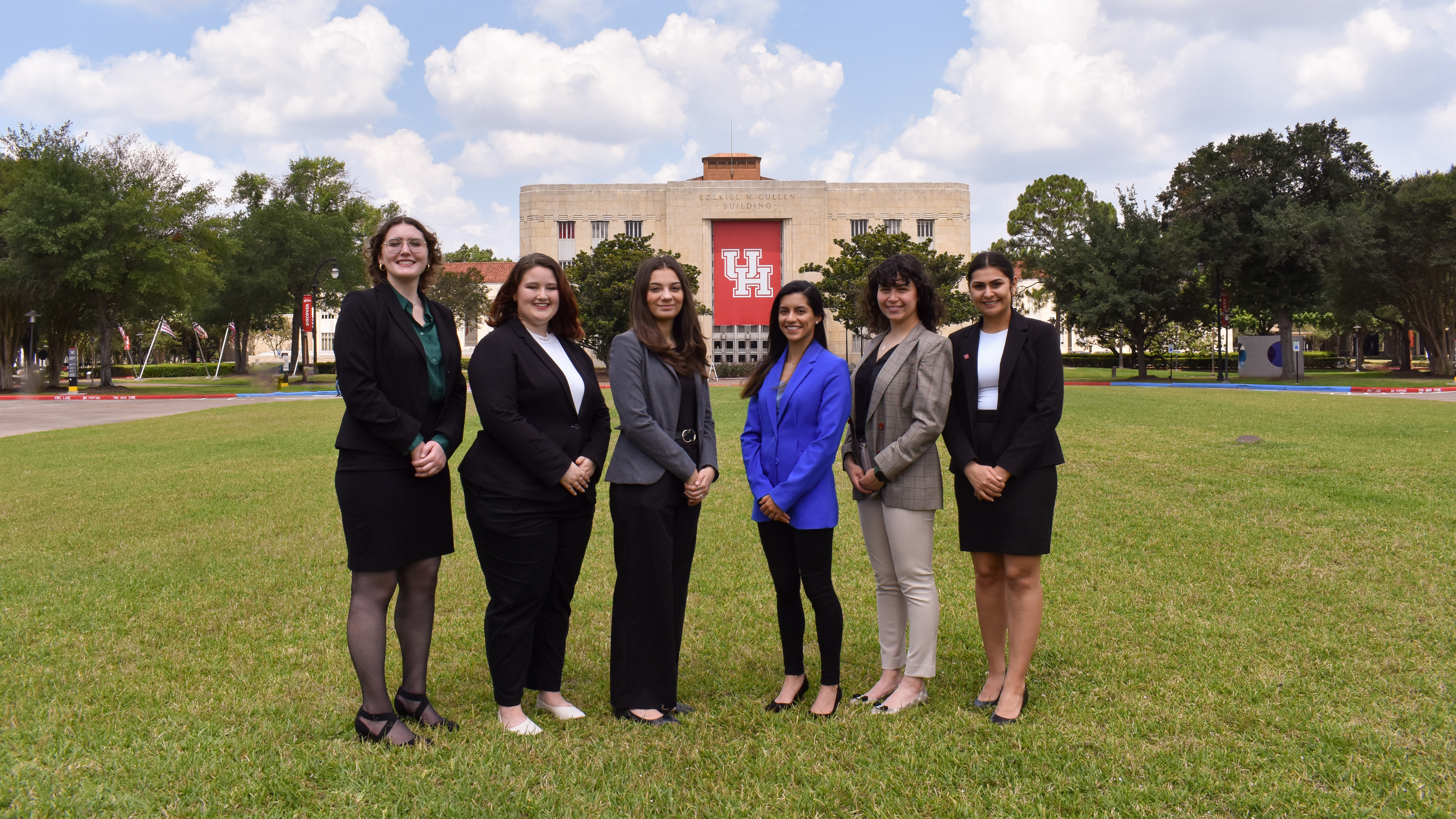 Six female college student standing in front of a UH banner