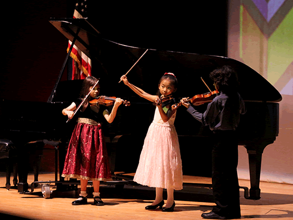 Young violin students performing on stage.