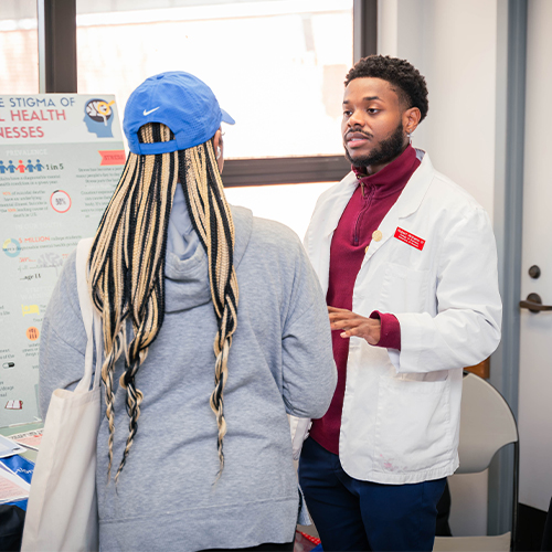 pharmacy student in white coat talks to patient at health fair