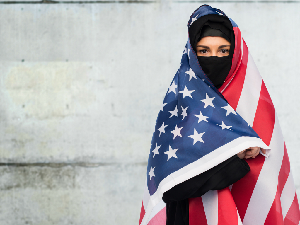 Muslim woman stands wrapped in American flag.