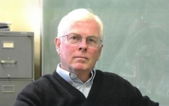 Photo of Dr. John McNamara sitting in front of a chalboard Photo of Dr. John McNamara sitting in front of a chalboard