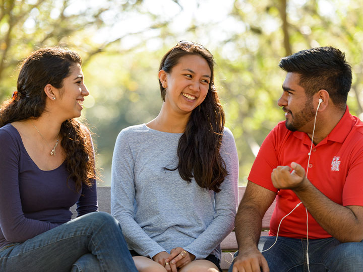 Three people sitting next to each other outside talking and smiling at each other.