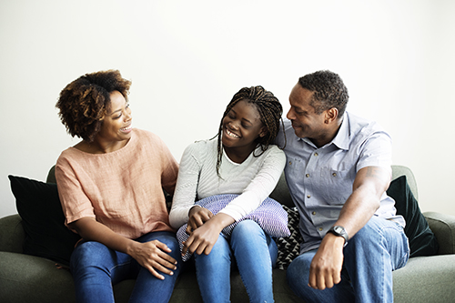 Black mother, teenager and father sitting on a couch smiling