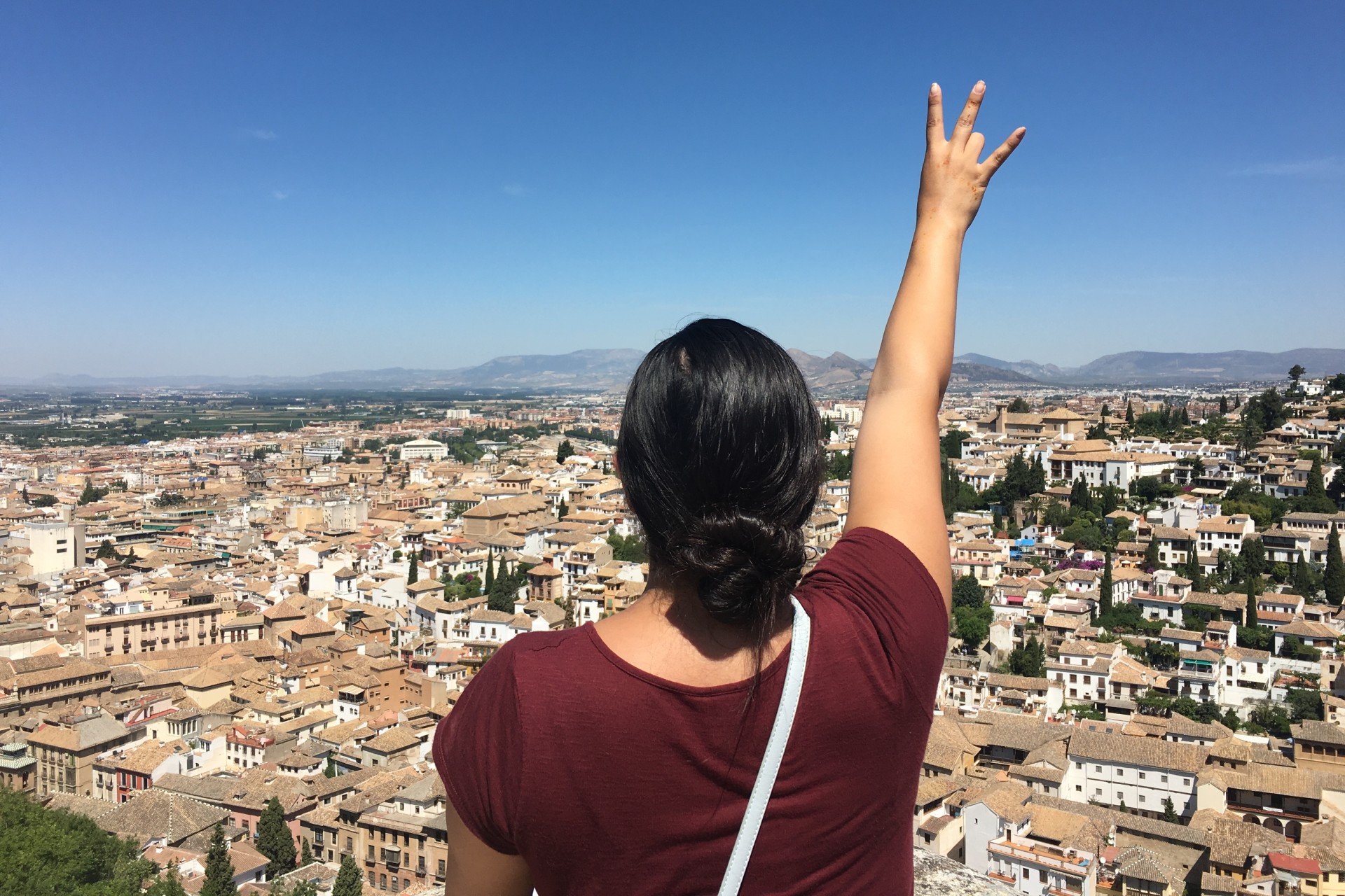 Photo of young woman holding up a UH Coogs sign overlooking a Western European city