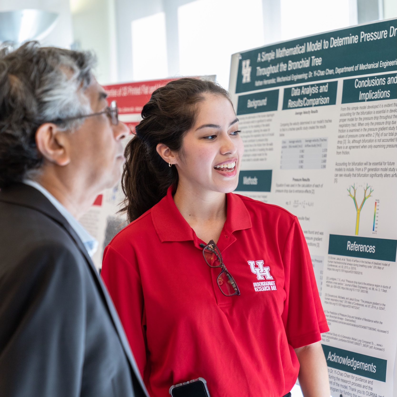 student talking to an Undergraduate Research Day visitor while looking at a research poster.