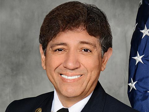 An image of a smiling man in uniform in front of an American flag.