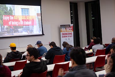 A crowded room of people watch a presentation about the Engineering Academy on a screen.