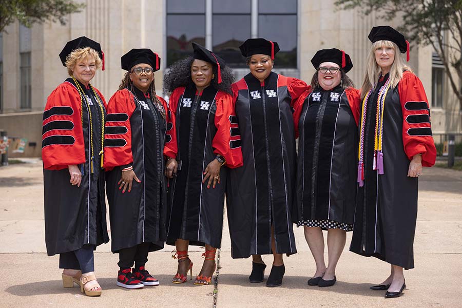 Photograph of a group of six women in red and black graduation regalia.
