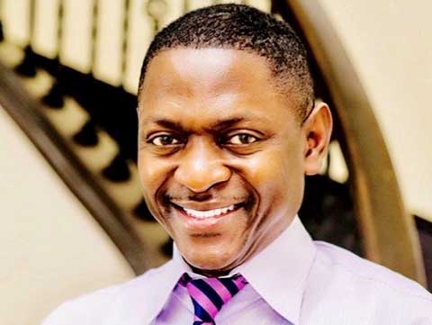 Portrait of a black man smiling wearing a light purple dress shirt and purple and black striped tie.