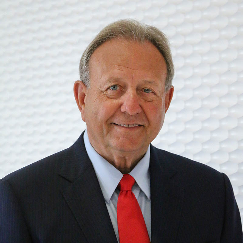 Portrait of man wearing a dark blue suit and a red tie.