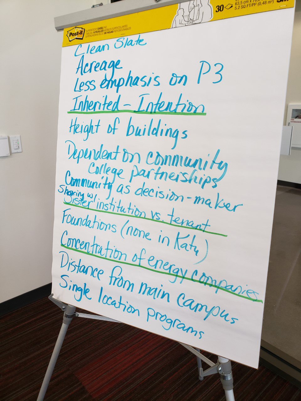 Large presentation post-its on a metal easel with handwritten notes about differences between the Katy and Sugar Land instructional sites