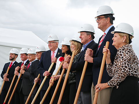 A group people wearing suits and hard hats holding shovels