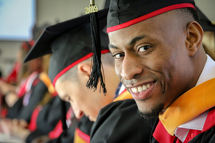 Close up a student wearing a graduation cap and gown looking at the camera.