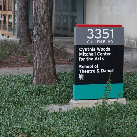 An outdoor sign surrounded by green ground cover reads from top to bottom: “3351 CULLEN BLVD.; Cynthia Woods Mitchell Center for the Arts; School of Theater & Dance; UH.” 