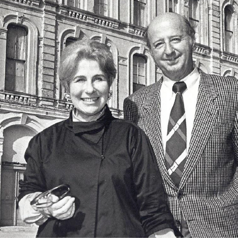 A historic, black and white photo of Cynthia Woods Mitchell and her husband in front of a building in daylight.