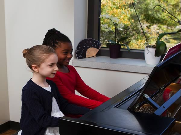 Two smiling little girls play the piano