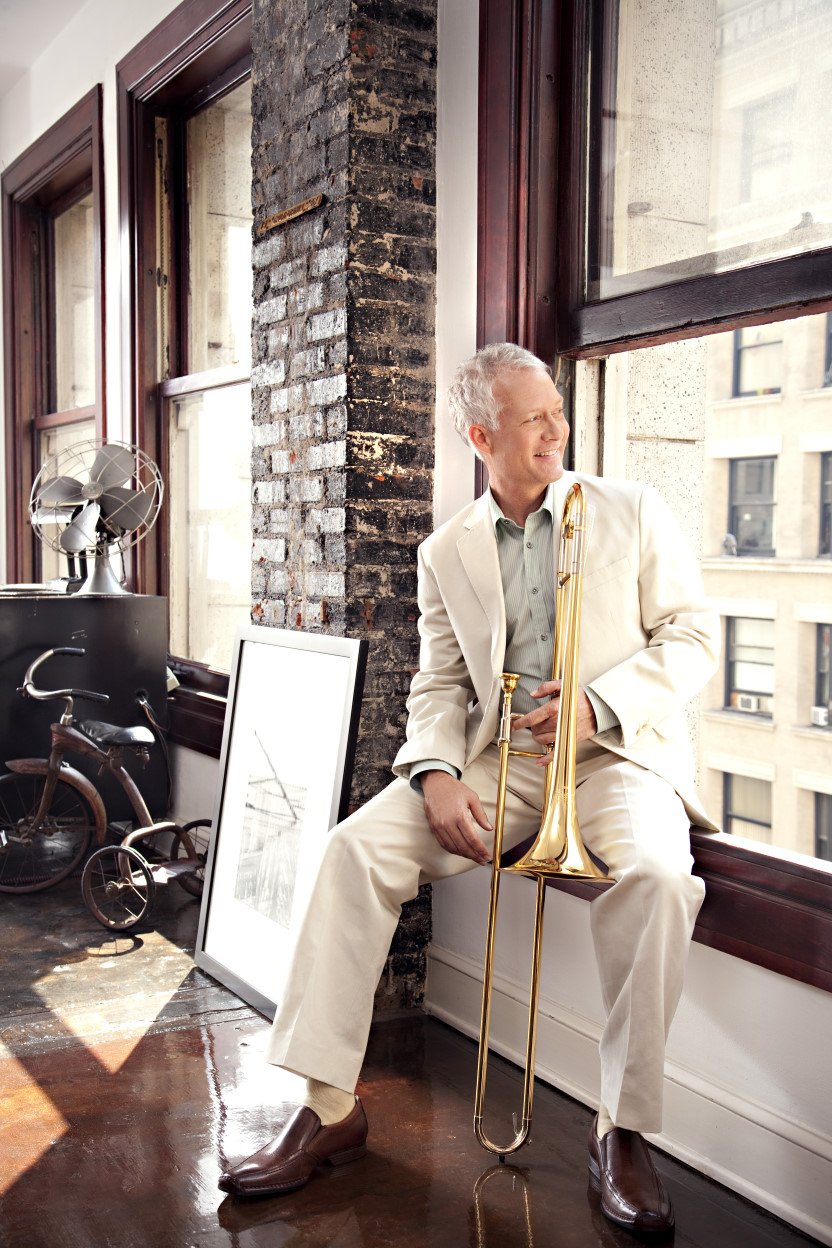 Photo of Andy Martin holding his trombone, smiling, and looking out a window