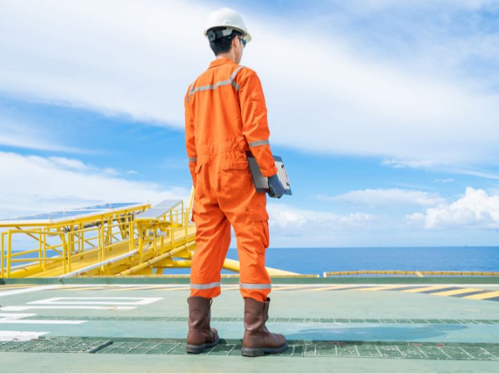 Man standing on offshore platform staring off into the distance at blue skies