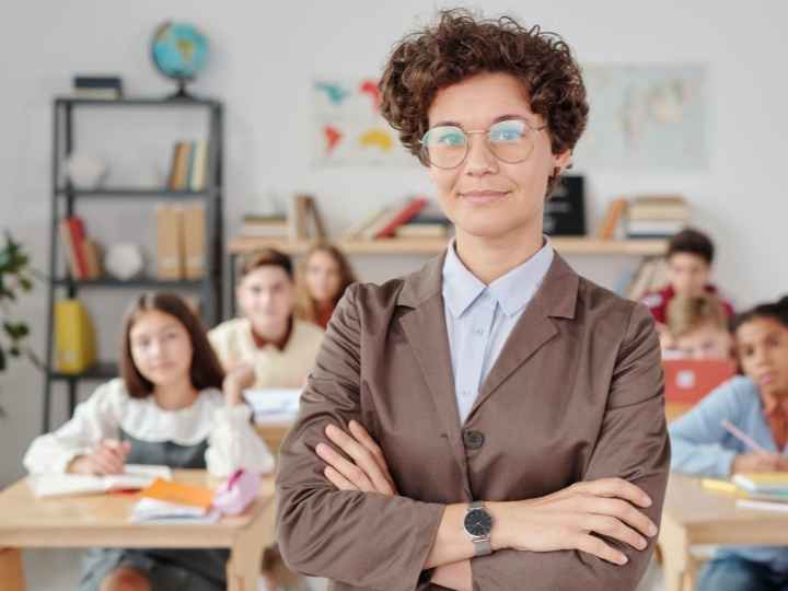 Photo of teacher standing, arms crossed, at head of class Photo of teacher standing, arms crossed, at head of class