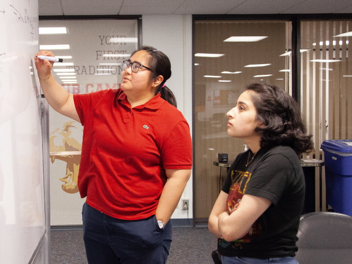 Reyna Isabel Diaz looks at a whiteboard which another student is writing on.