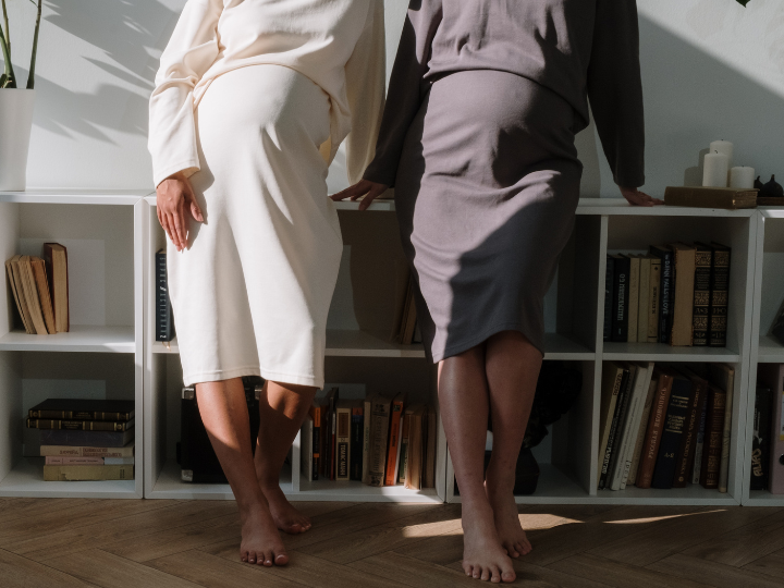 Two pregnant women stand side by side facing camera Two pregnant women stand side by side facing camera