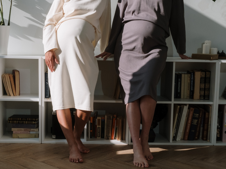 Two pregnant women stand side by side facing camera