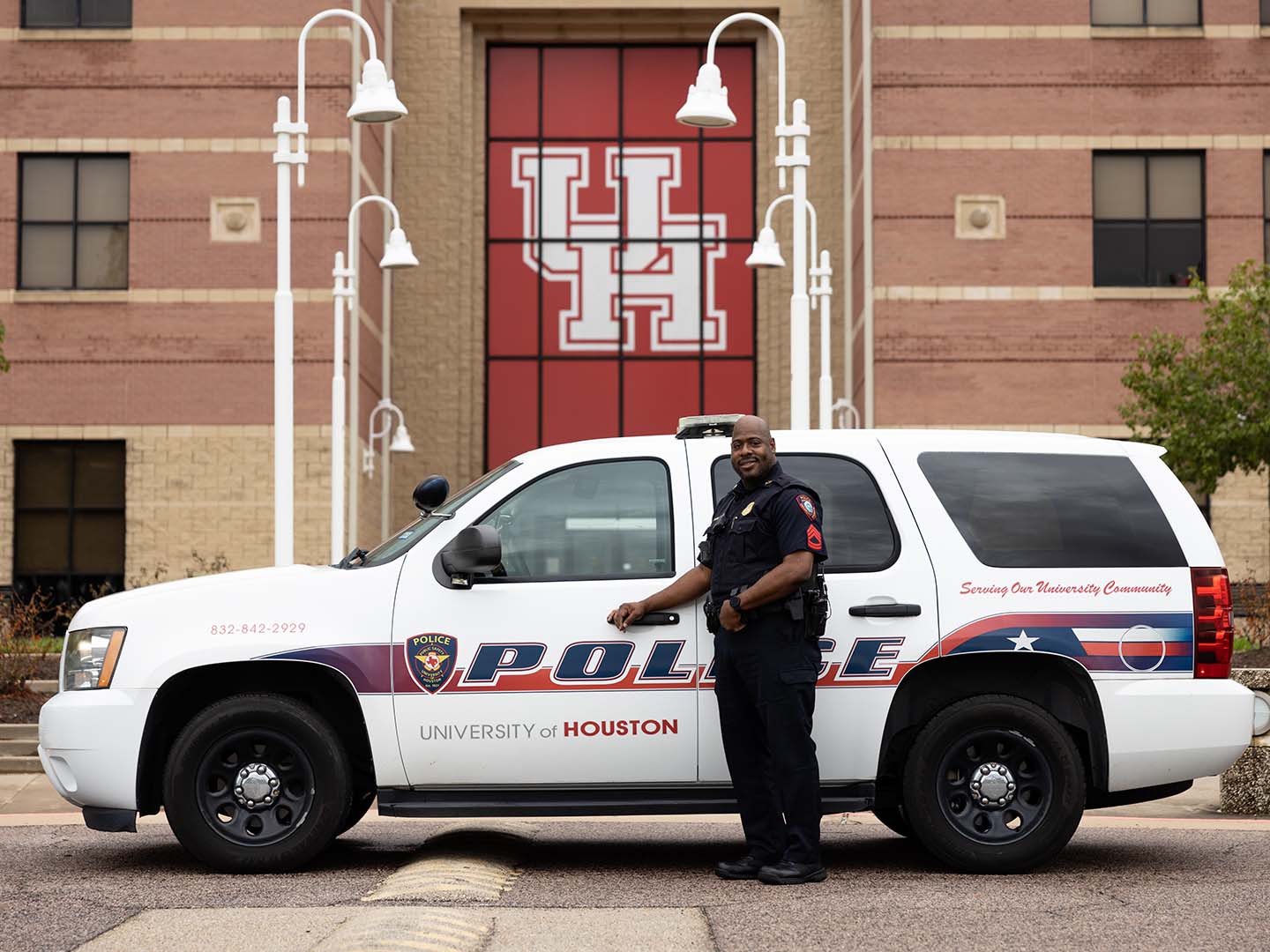 UH police officer standing next to police car.