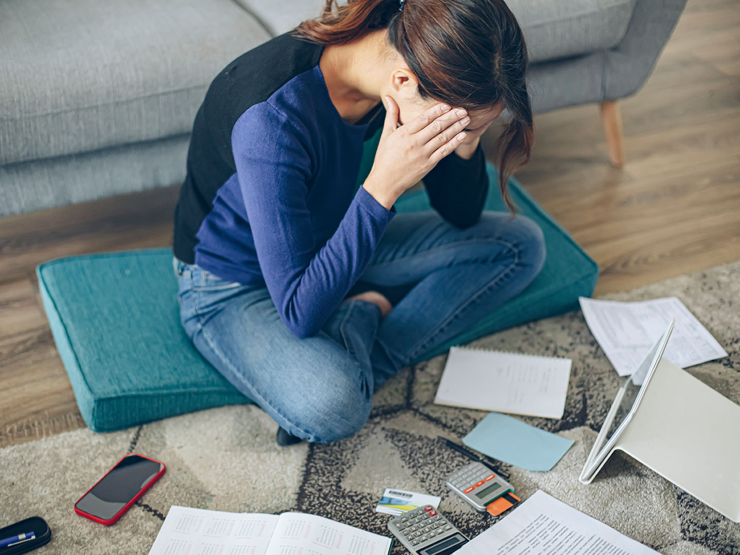person sitting on floor, looking stressed while surrounded by bills