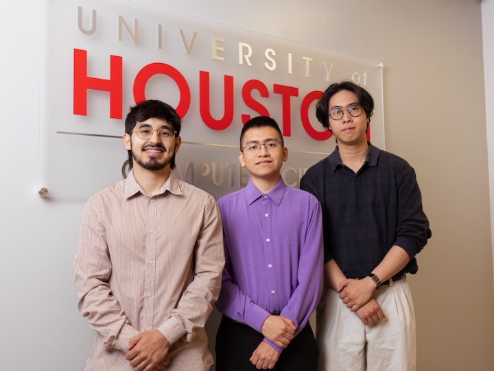 Three students stand smiling in front of a University of Houston computer science sign.