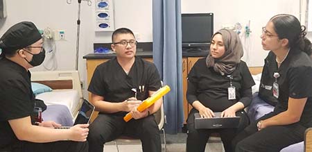 A group of nursing students wearing black scrubs sit together in discussion..