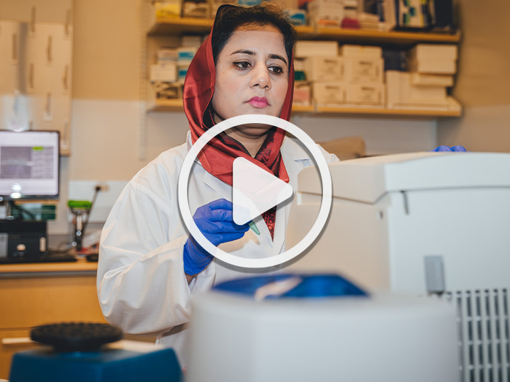 Sana Sharif in laboratory with a play button to designate this image links to a video