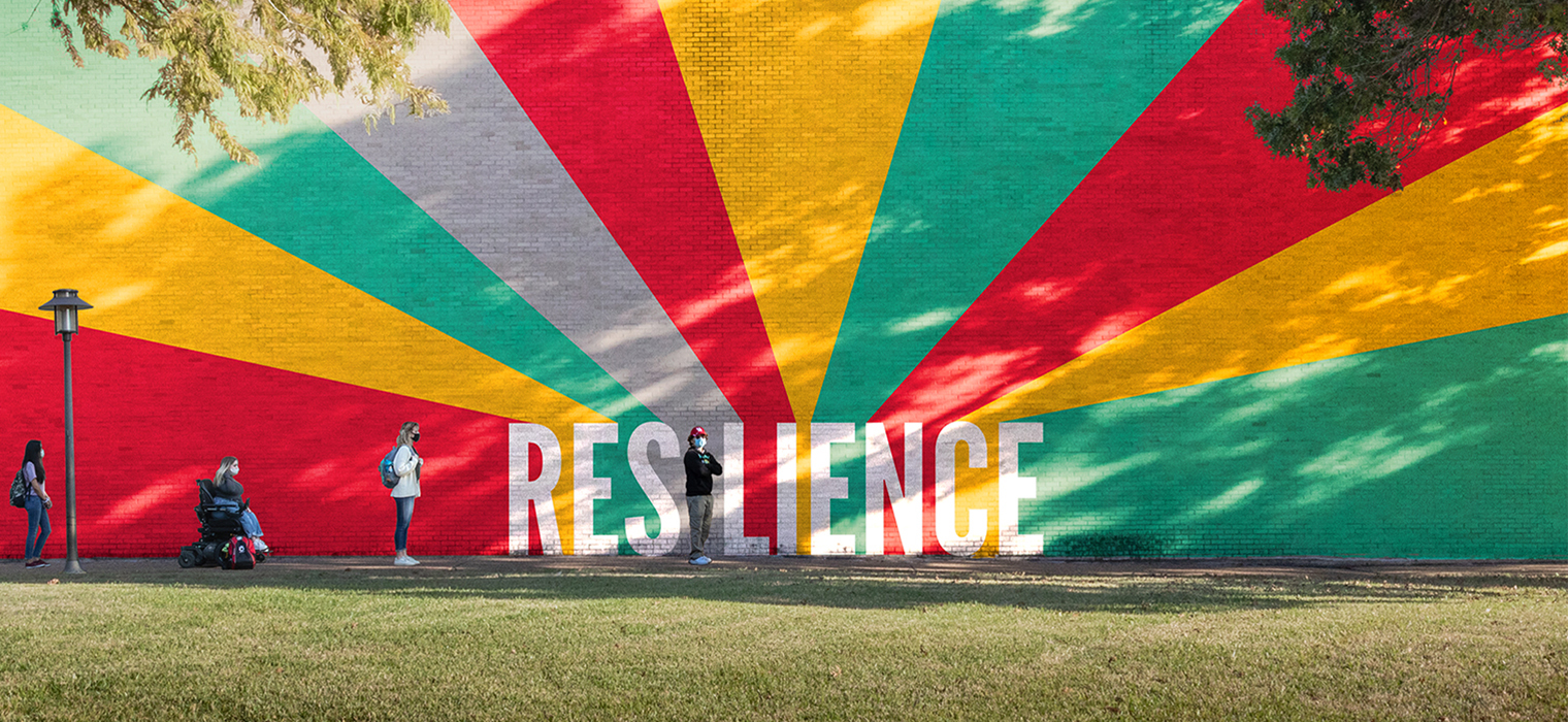 Masked students standing in socially-distanced line against a wall that says Resilience
