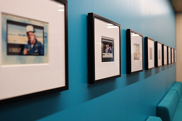 A different angle of a collection of framed digital ink prints on a blue wall