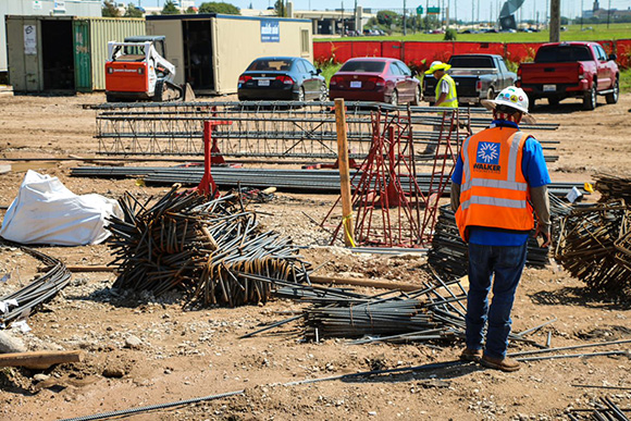 A construction worker walking towards a pile of reinforcing bars on the ground