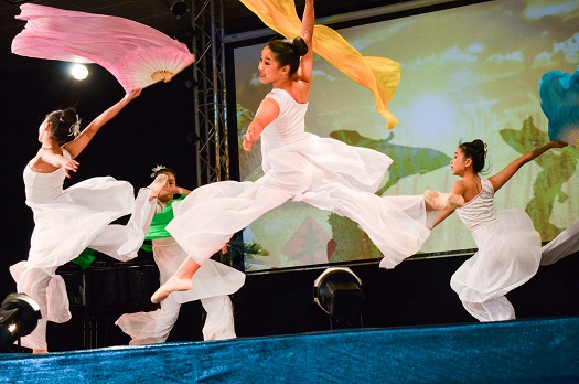 Four female dancers in white twirl colored streamers on stage