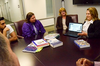 Instructors and students in discussion while seated at a conference table