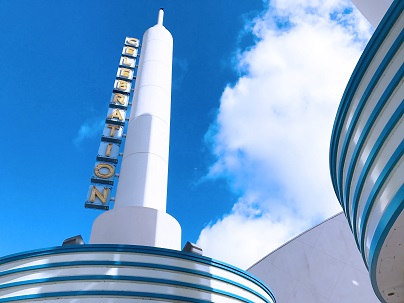 A vertical marquee on a white tower against a blue sky with large downy clouds