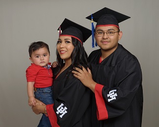 A hispanic couple in graduation regalia holding a young toddler