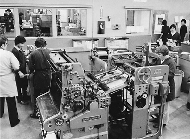 Old black and white photo of a group of students and an instructor using large printing equipment