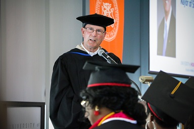 A man wearing glasses at a podium speaks to graduates
