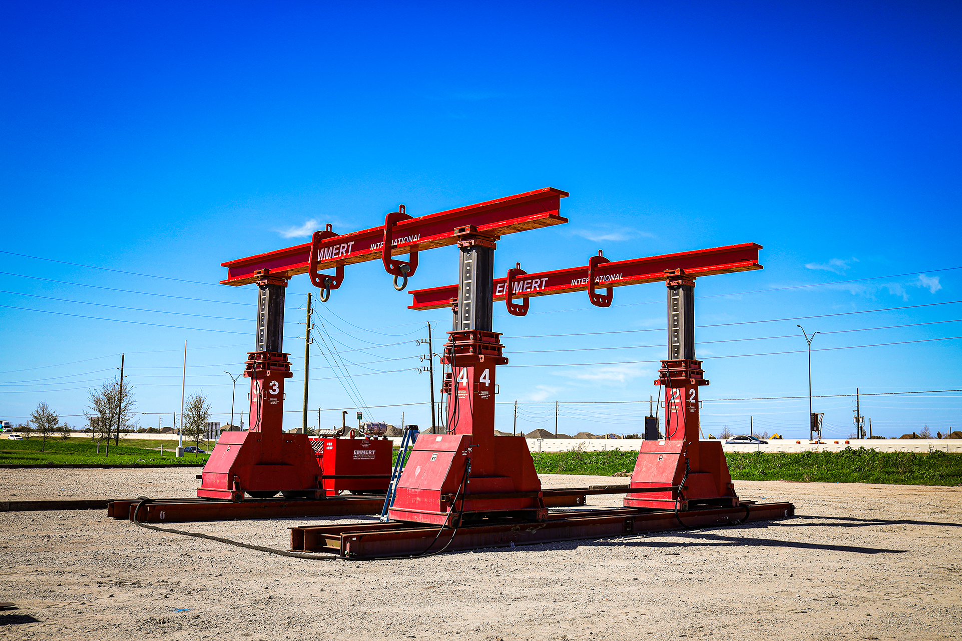 A pair of large red mobile lifts that can extend a horizontal red beam with large sets of fastening rings