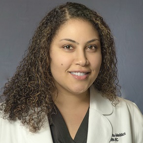 Portrait of a woman with brown curly hair smiling in a labcoat