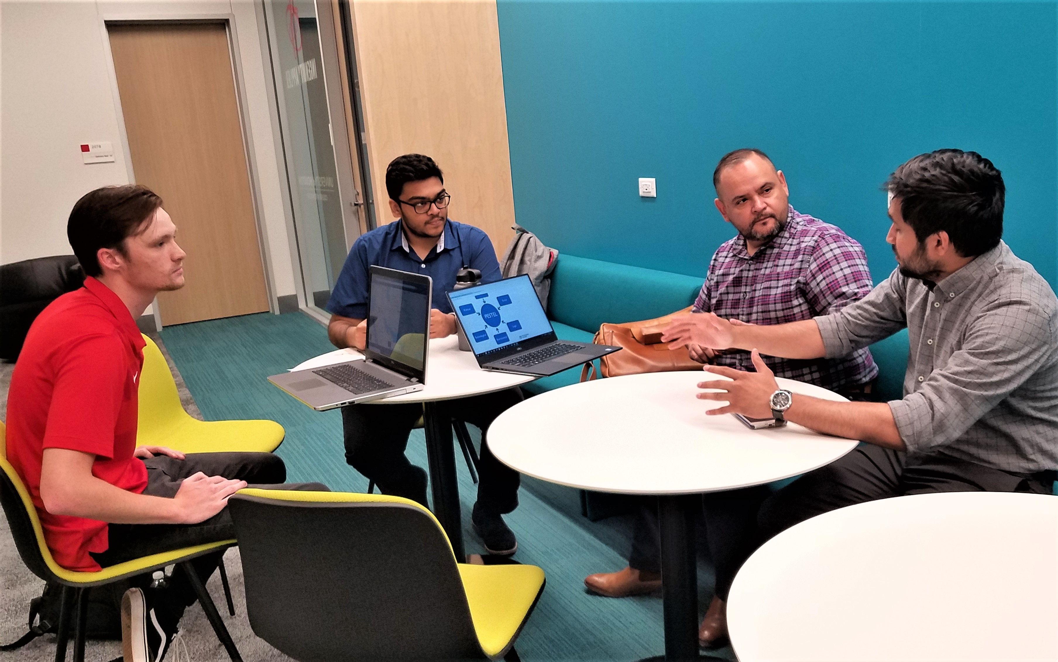 Four people in a discussion sit a round tables in a lounge.