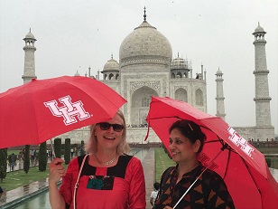 Two women holding umbrellas with a large ivory-white marble Islamic mausoleum in the background