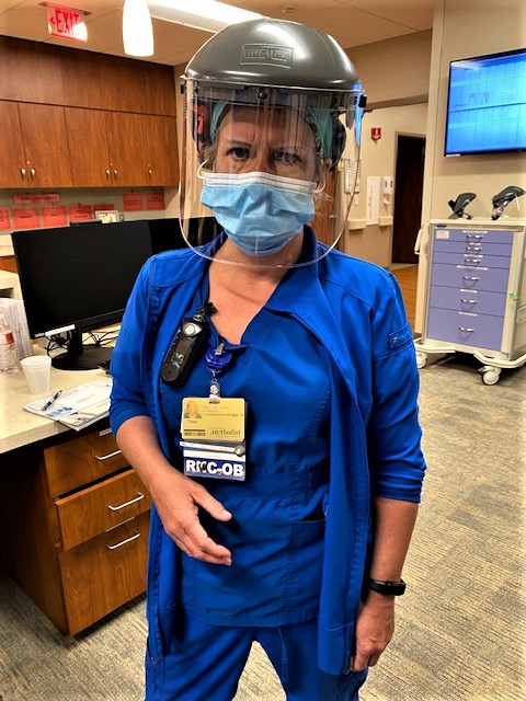 A woman in blue scrubs wearing personal protective equipment on her head and face