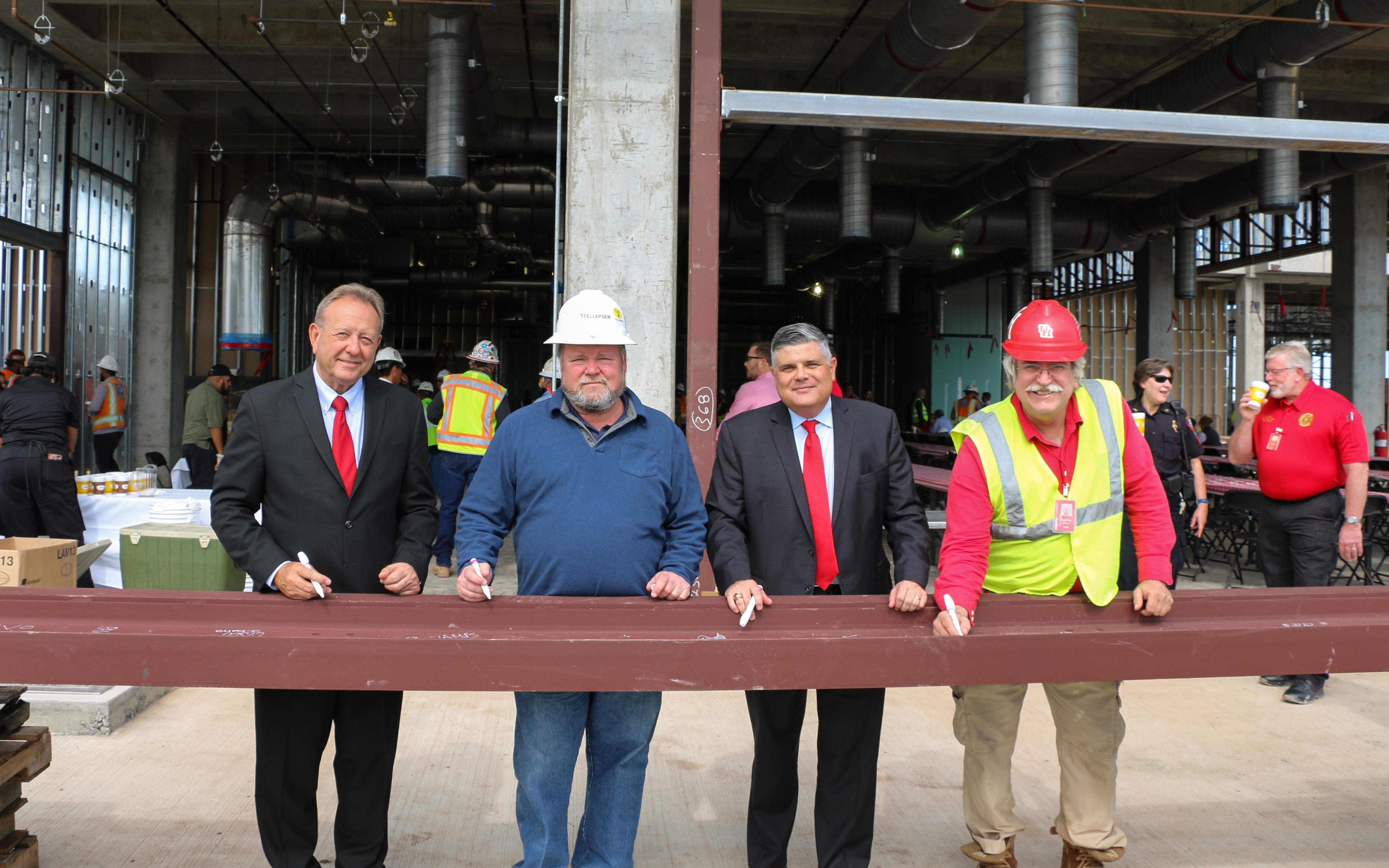 Two men in suits and two men in construction outfits signing a metal girder