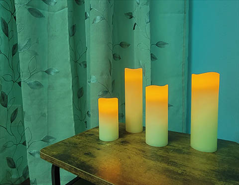 A wooden table with four electronic candles against a sea-green wall and a green curtain.