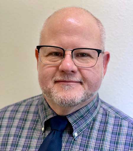 Portrait of an older white man with a short white and grey beard and wearing glasses.