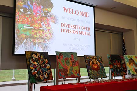 Several pieces of artwork on easels are in front of a large projection screen with a welcome message.