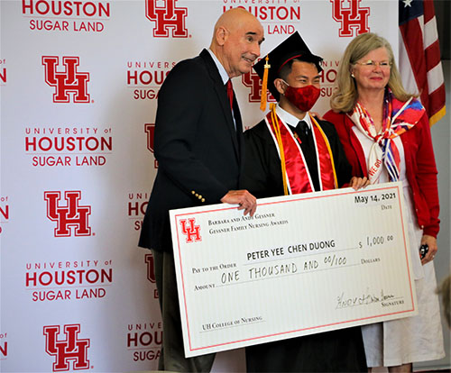 A man and a woman flank a Nursing graduate holding a large novelty-sized check.